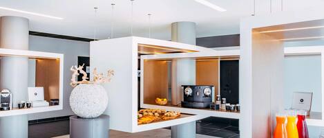Un vestíbulo de hotel moderno con un mostrador de recepción, máquinas de café y una exposición de fruta.