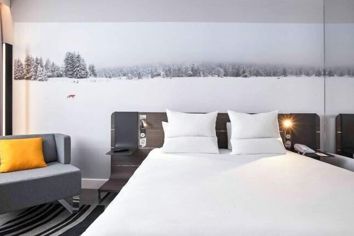 Una habitación de hotel moderna con una cama grande, un sofá y una mesita de noche.