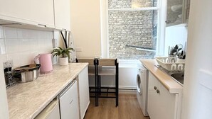 A compact kitchen with white cabinetry, a wooden floor, a window with a brick wall, and a washing machine.