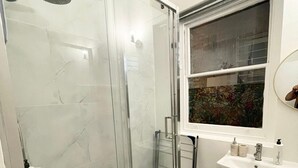 A modern bathroom with a glass-enclosed shower, a vanity with a sink, and a window above the mirror.