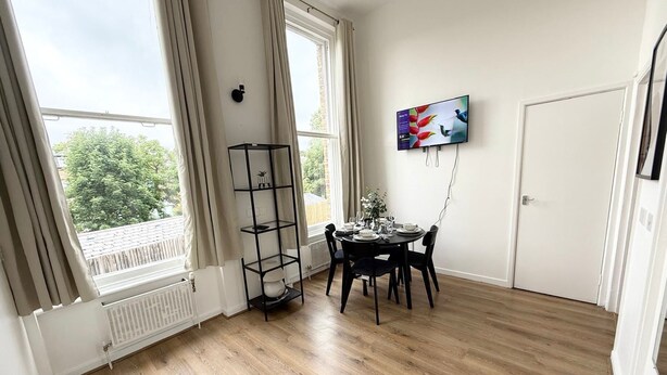 A room with a dining table set for four, a black metal shelf, and a painting on the wall.