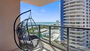 Un balcon avec un fauteuil suspendu donnant sur une plage et un immeuble de grande hauteur.