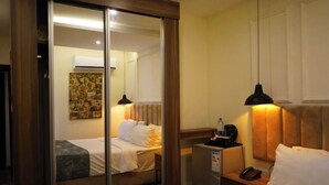 Ein Hotelzimmer mit Bett, Nachttisch, Lampe und einem Spiegel, der den Raum widerzuspiegeln scheint.