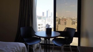 Ein Hotelzimmer mit einem Bett, zwei Stühlen, einem kleinen Tisch und einem großen Fenster mit Blick auf die Stadt.