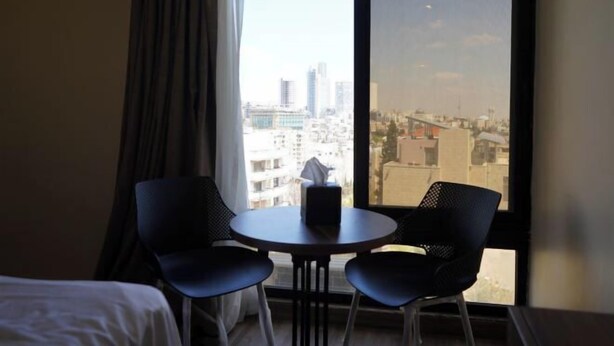 A hotel room with a bed, two chairs, a small table, and a large window offering a city view. - Post Boutique Hotel Amman (Amman)