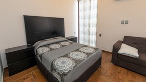 A bedroom with a bed, a nightstand, a TV, a window with curtains, and a sofa. - Hotel Rivas  (Tequila)