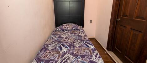 Una habitación pequeña y estrecha con una cama individual y un edredón estampado.
