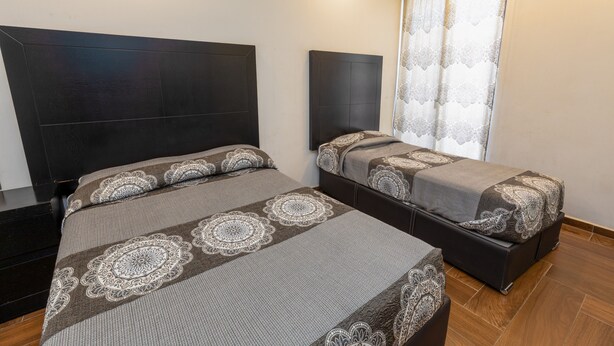 A hotel room with two beds, a large headboard, a window with curtains, and a wooden floor. - Hotel Rivas  (Tequila)