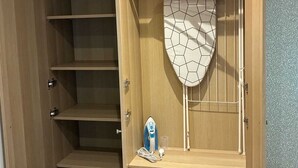Een houten garderobe met meerdere planken en een hanggedeelte, een ronde spiegel, en een klein strijkplank.
