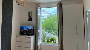 Ein Zimmer mit Fernseher auf einer Kommode, einer Hängeleuchte und einem Fenster mit Vorhängen.