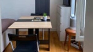 Ein kleiner, kompakter Raum mit einem Einzelbett, einem Schreibtisch und einem Stuhl. Ein kleiner Tisch mit einer Pflanze und ein Fernseher auf einem Standfuß.