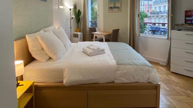 A hotel room with a large bed, a desk, a chair, and a view of buildings through the window. - Studio number 6 in Pantin (Pantin)