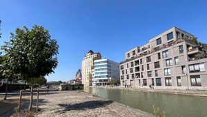 A riverside promenade with cobblestone pavement, modern buildings, and a tree. - Studio number 6 in Pantin (Pantin)