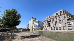 Een promenade langs de rivier met geplaveid pad, een boom en moderne gebouwen met balkons.