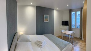 Een hotelkamer met een bed, een bureau, een stoel, een televisie en een raam met uitzicht op gebouwen.