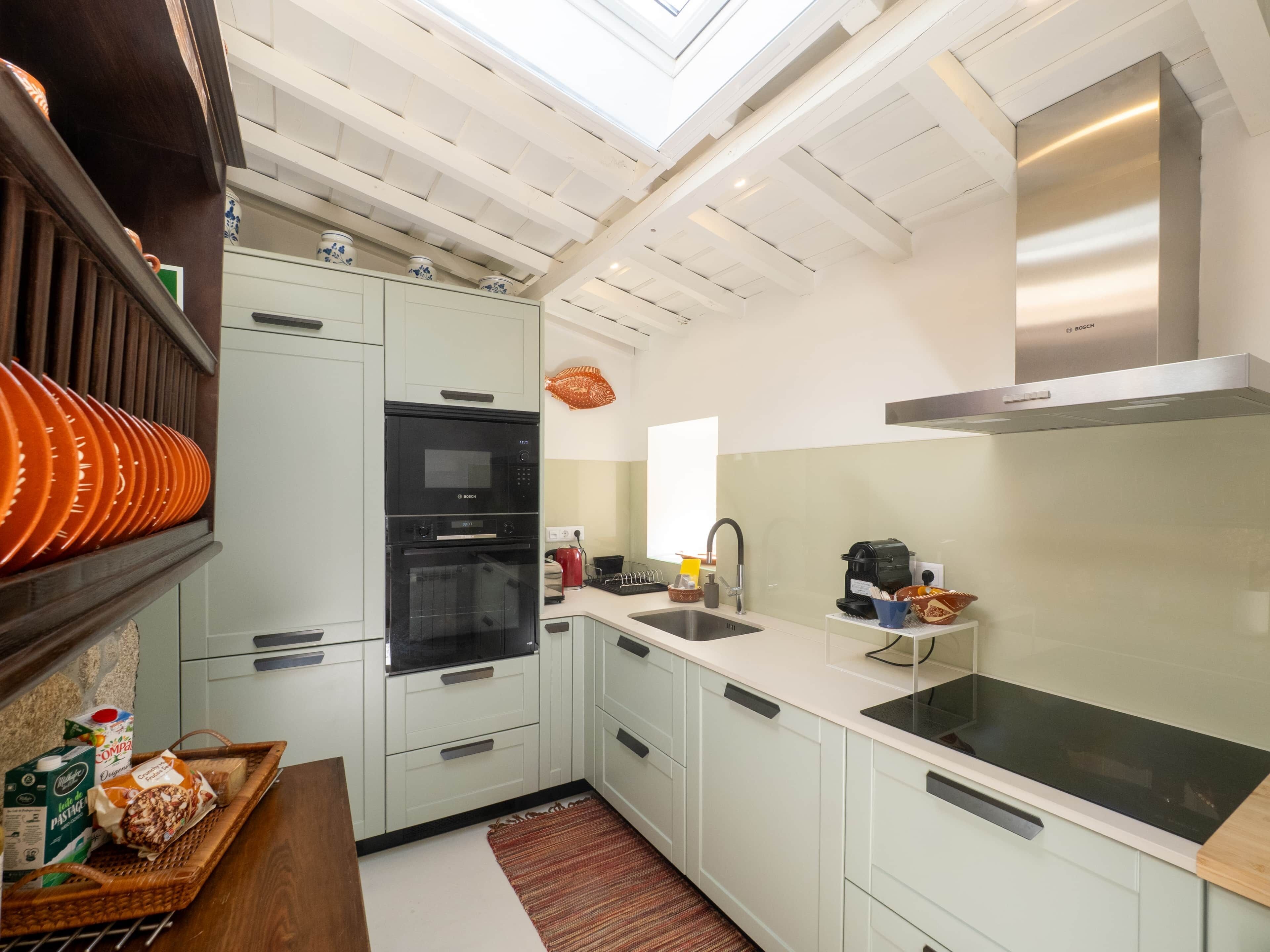 A modern kitchen with white cabinets, a Bosch oven, a stainless steel range hood, and a skylight.