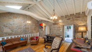 Une pièce chaleureuse avec un mur en pierre, des poutres en bois au plafond, un canapé en cuir marron, un fauteuil à bascule et une table à manger.