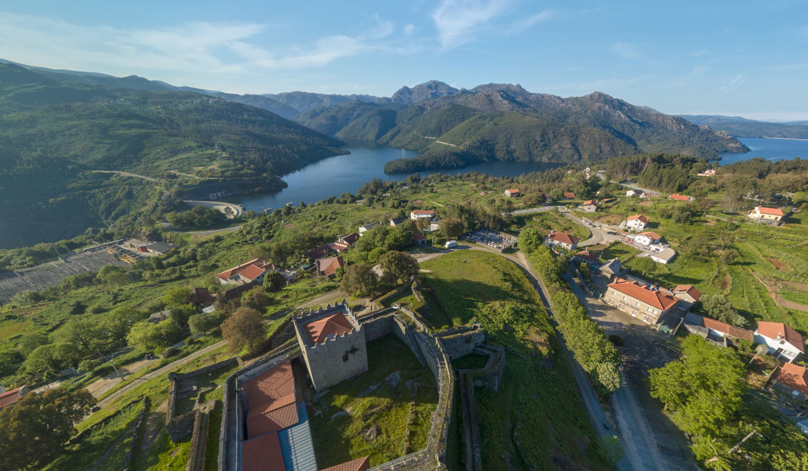 Une vue aérienne d’une ville historique, avec un château, entourée de collines verdoyantes et d’un lac.