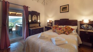 Une chambre à coucher avec un grand lit, une commode en bois, une table de chevet, un miroir et une fenêtre avec des rideaux.
