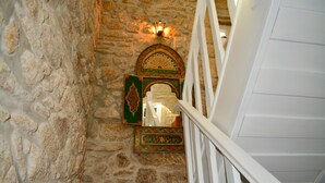 Un escalier en pierre avec une rampe blanche, une porte décorative ornée de motifs complexes et un luminaire fixé au mur.