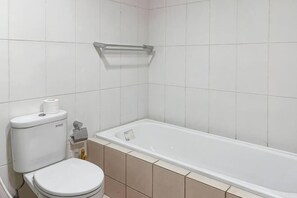 A bathroom with a toilet, a bathtub, and a shelf above the toilet.
