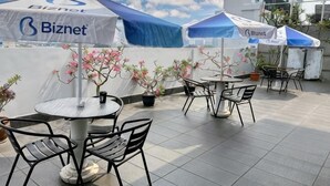 Een terras op het dak met buitenmeubilair, overdekt met blauw-witte parasols, en met planten in potten.