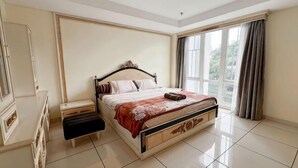 Een slaapkamer met een bed, nachtkastje, dressoir en grote ramen.