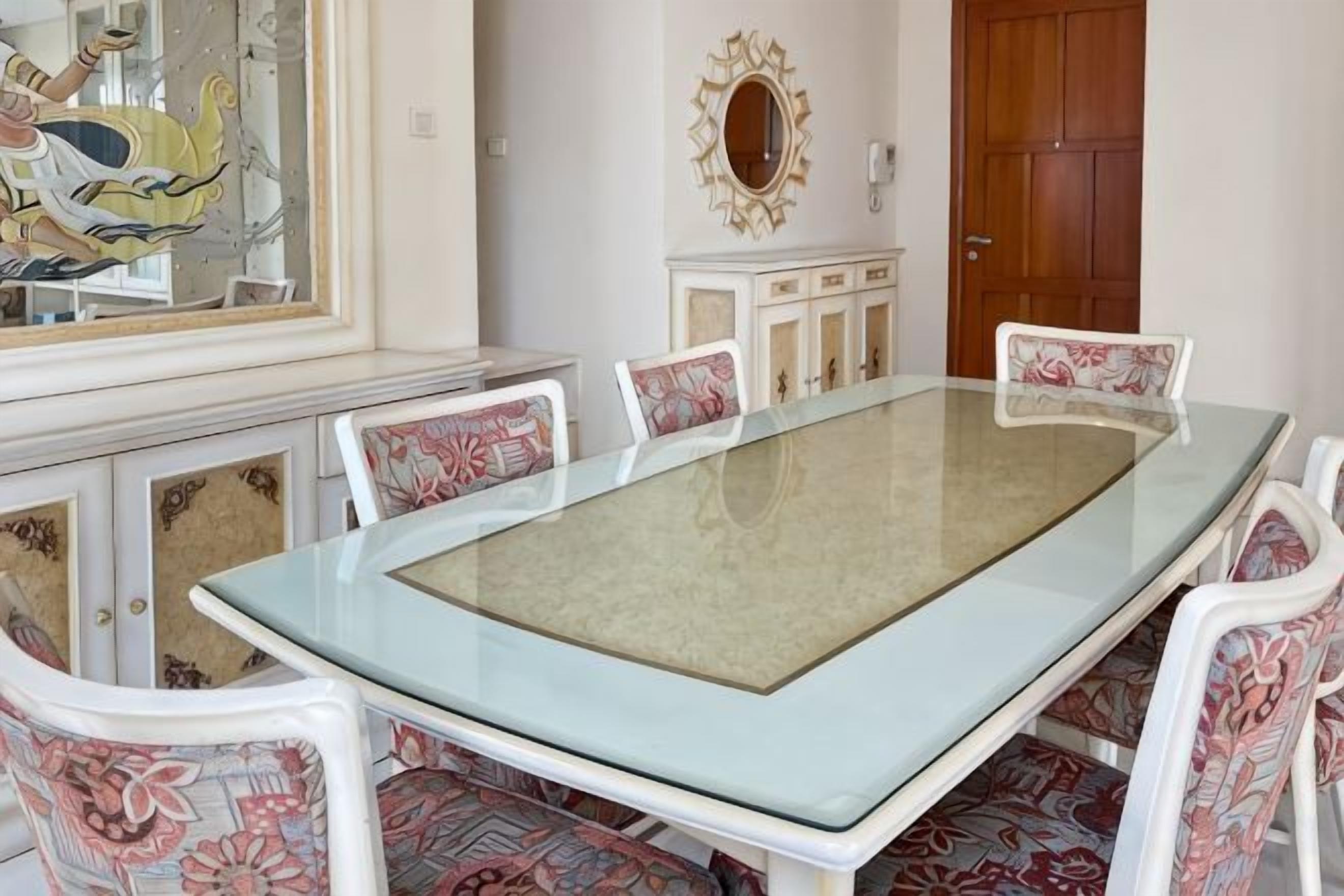 Un coin repas avec une table à plateau en verre, entourée de chaises à motifs, une porte en bois et un miroir décoratif.