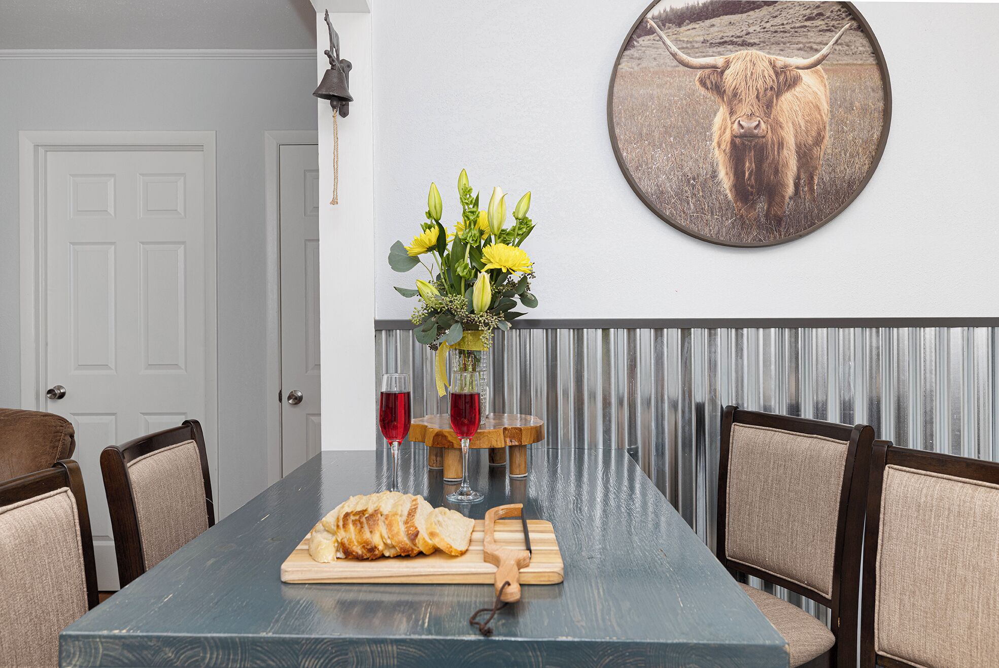 Ein Essbereich mit einem langen Tisch, Stühlen, einer Vase mit Blumen und einem gerahmten Bild an der Wand.