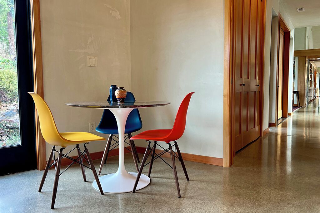 A modern interior with a round table and colorful chairs, a vase, and a view of a hallway.