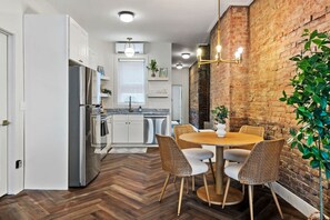 A modern kitchen with white cabinets, a stainless steel refrigerator, and a dining area with wicker chairs and a round table.