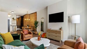 A modern living room with a green sofa, a brown armchair, and a white coffee table. There is a TV mounted on the wall and a small side table with a lamp. - 2615 Jane Down - Southside (Pittsburgh)