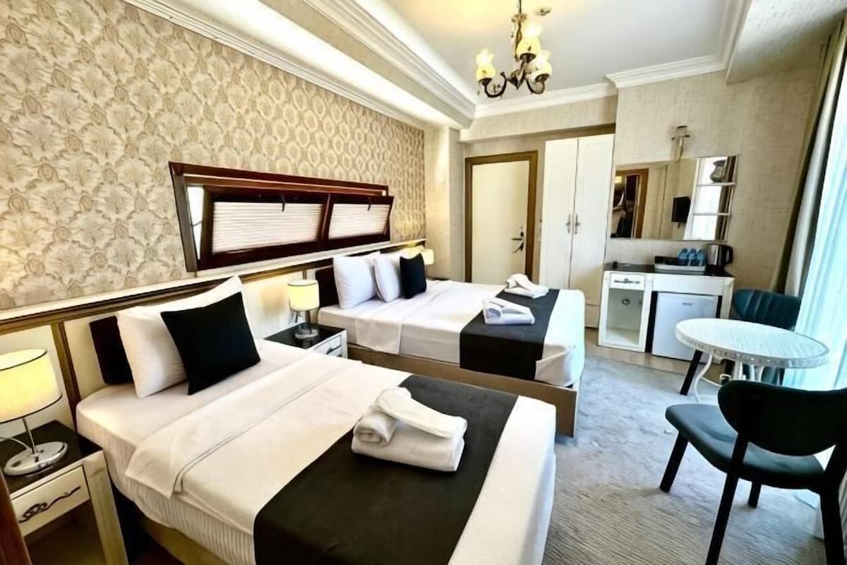 A hotel room with two beds, a desk, a chair, a small table, and a kitchenette.