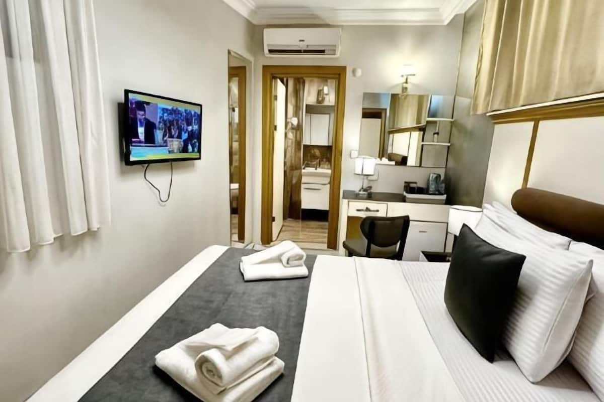 A hotel room with a bed, a desk, a television, and a bathroom visible through an open door.