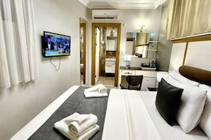 Una habitación de hotel con una cama, un escritorio, televisión y un baño visible a través de una puerta abierta.