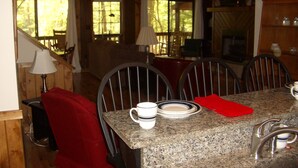 A dining area with a granite table, chairs, and a red throw pillow. There is a chandelier, a fireplace, and a view of the outdoors through large windows. - A CABIN ON PARADISE Tranquil cabin in Murphy - just 1 mile from JCC Folkschool (Murphy)