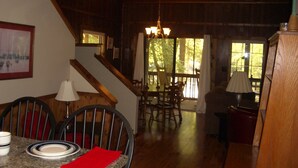 A dining area with a table set for two, a staircase leading to another level, and a view of the outdoors through large windows. - A CABIN ON PARADISE Tranquil cabin in Murphy - just 1 mile from JCC Folkschool (Murphy)