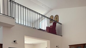 En rummelig spiseafdeling med et stort træbord og stole, et køkken i baggrunden og en balkon med gelænder.
