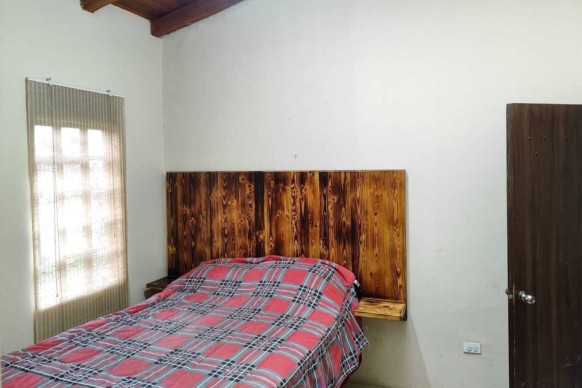 Een slaapkamer met een houten hoofdeinde, een geruit sprei, een raam met zonwering en een deur.