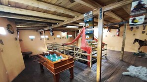 Una habitación con techo de madera, una mesa de fútbol de mesa, una estructura roja para escalar y una estatua de caballo.