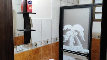 Une salle de bain avec des toilettes, un lavabo et une douche. On trouve des articles de toilette sur une étagère.