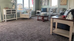 A living room with a patterned armchair, a striped sofa, a coffee table, and a small white cabinet with drawers.