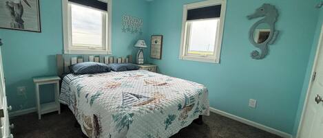 A bedroom with a bed, two nightstands, a ceiling fan, two windows, and a seahorse decoration.