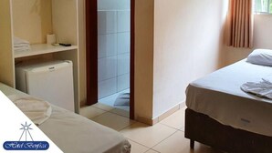 A hotel room with a bed, a wardrobe, a small fridge, and a door leading to a tiled area. - Hotel Benfica (Aparecida)