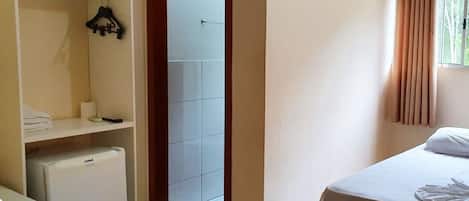 Quarto de hotel com cama, guarda-roupa, mini-frigorífico e porta para área com azulejos.