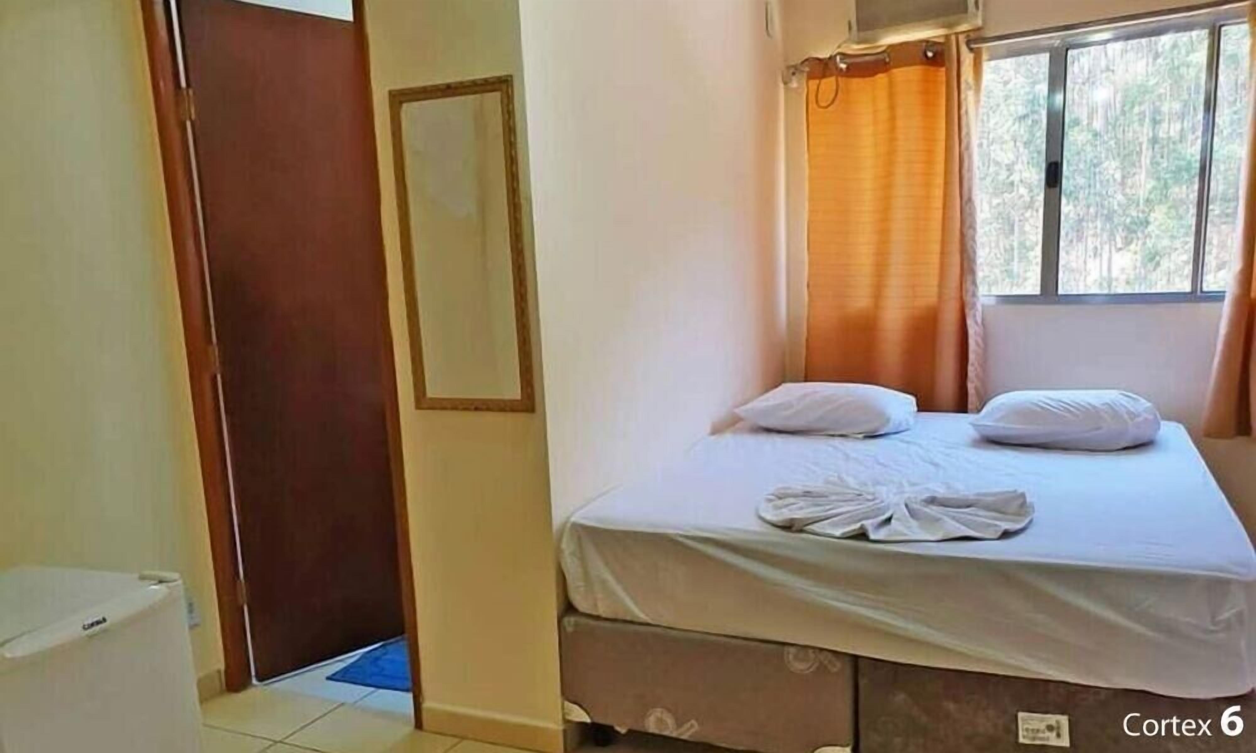 Een slaapkamer met een bed, een raam met gordijnen, een deur en een klein raam met uitzicht op bomen.