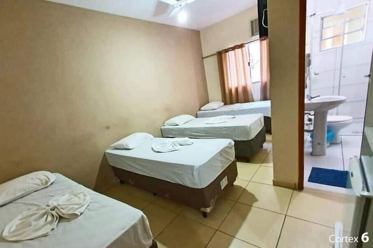 Habitación de hotel con tres camas, un baño que incluye lavamanos e inodoro, y un ventilador de techo.