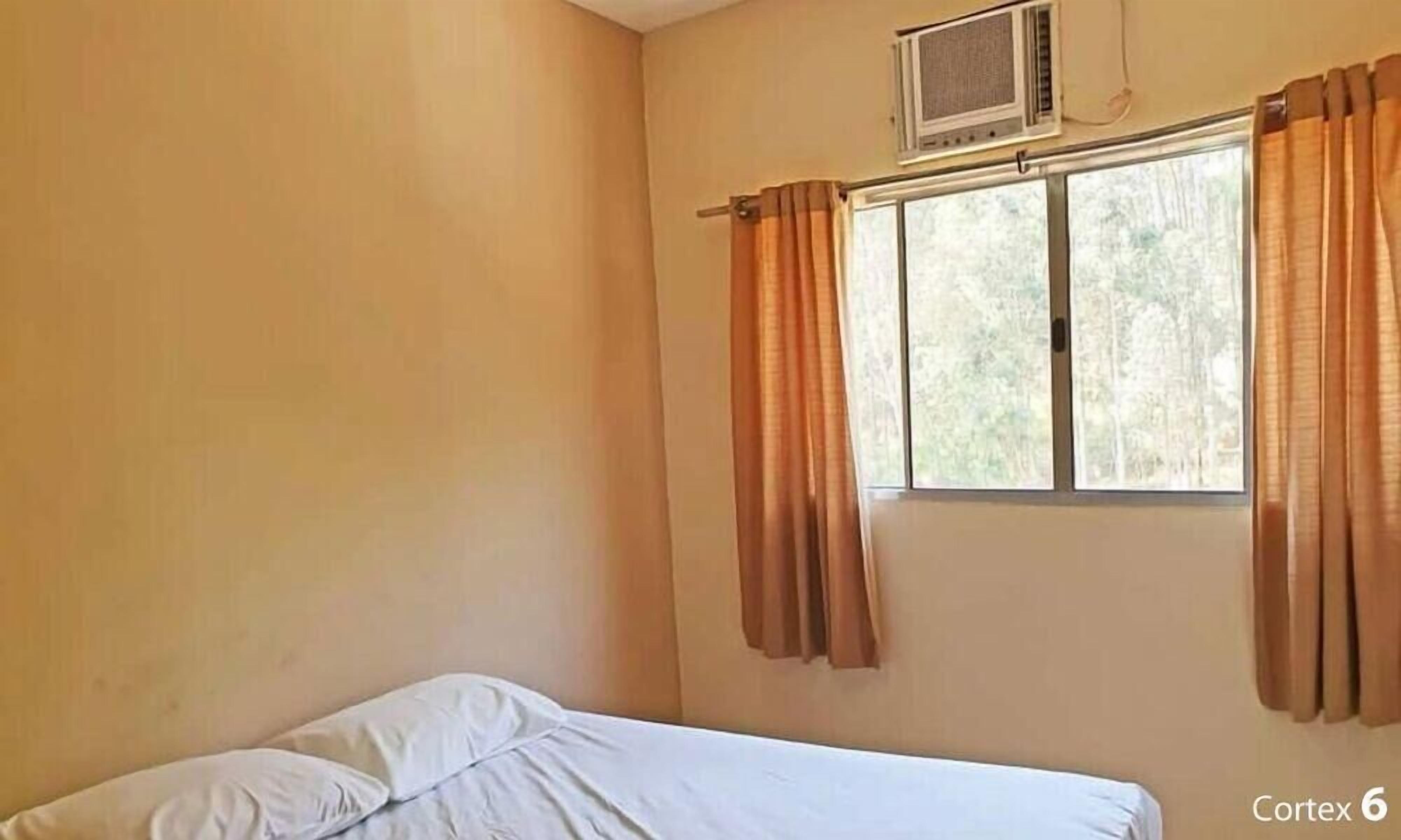 A room with a bed, a window with curtains, and an air conditioning unit on the wall.