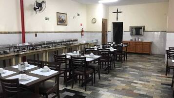 Un comedor con varias mesas y sillas, un reloj en la pared y una cruz.