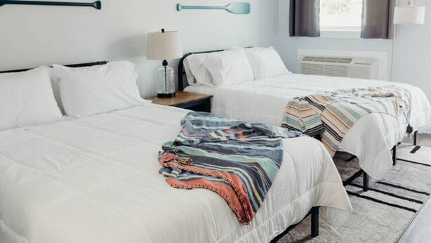 A modern bedroom with two beds, a large window with curtains, and wall-mounted paddleboards. - The Pendergrass Room, Lakeside Inn at Dale Hollow (Monroe)